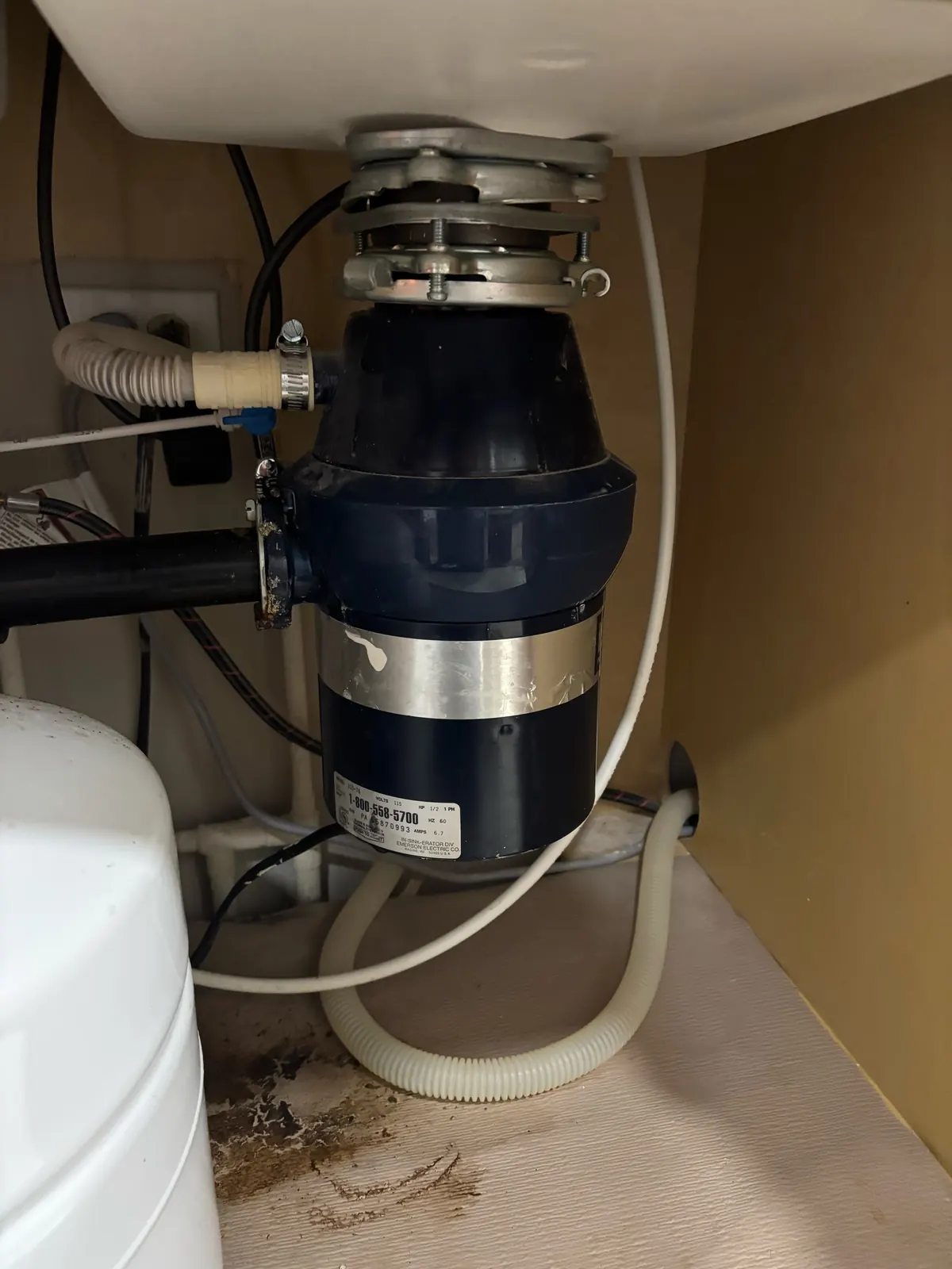 Old garbage disposal under a kitchen sink before replacement